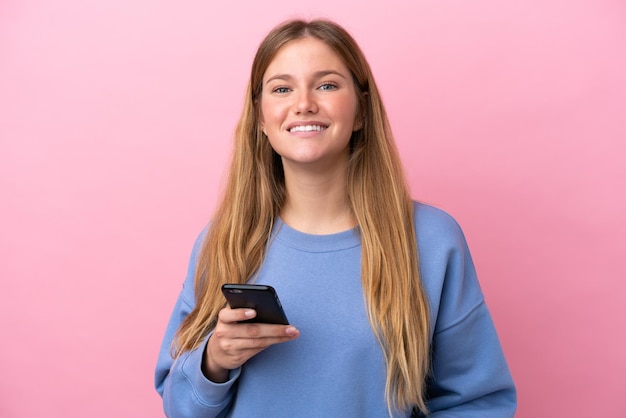 Jonge blonde vrouw geïsoleerd op roze achtergrond met behulp van mobiele telefoon