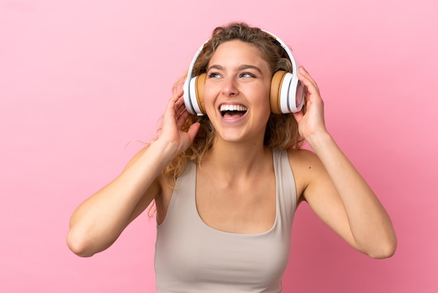Jonge blonde vrouw geïsoleerd op roze achtergrond muziek luisteren en zingen