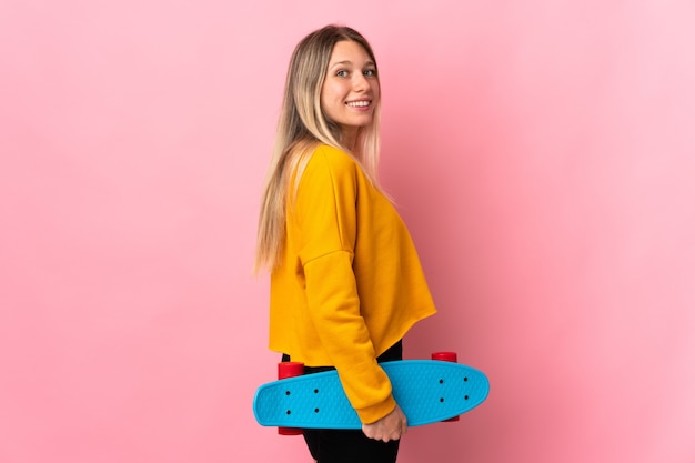 Jonge blonde vrouw geïsoleerd op roze met een skate