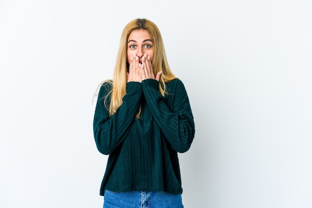 Jonge blonde vrouw geschokt die mond met handen bedekken.