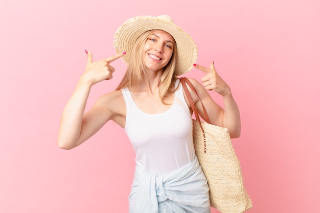 Jonge blonde vrouw glimlachend vol vertrouwen wijzend naar eigen brede glimlach