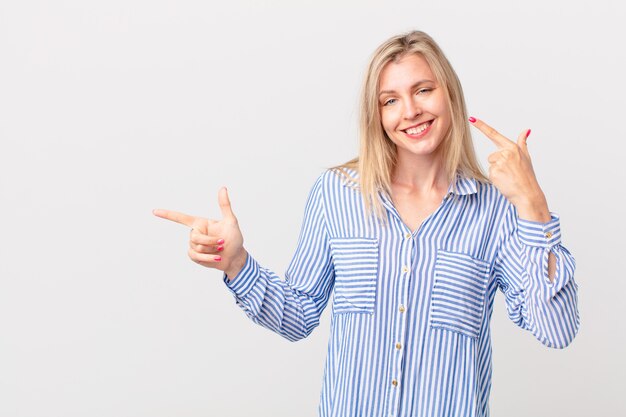 Jonge blonde vrouw glimlachend vol vertrouwen wijzend naar eigen brede glimlach