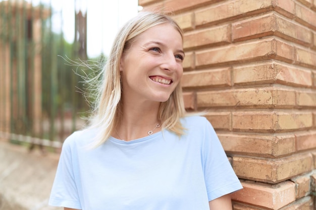 Jonge blonde vrouw glimlachend zelfverzekerd kijkend naar de zijkant op straat