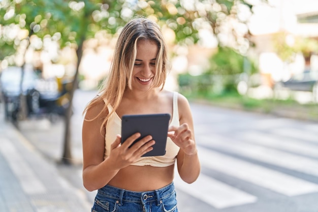 Jonge blonde vrouw glimlachend zelfverzekerd met behulp van touchpad op straat