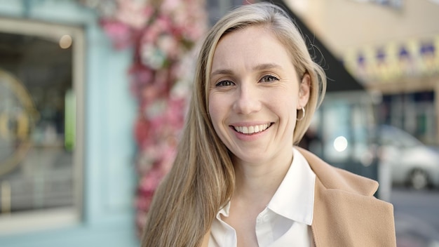 Jonge blonde vrouw glimlachend zelfverzekerd staande op het terras van de coffeeshop