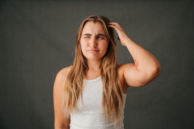 Jonge blonde vrouw haar hoofd krabben en denken