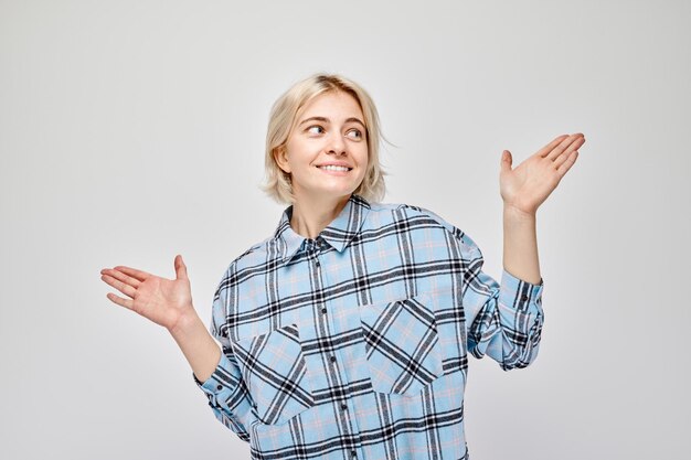 Foto jonge blonde vrouw in casual houdt iets in de hand en demonstreert lege ruimte voor product of tekst geïsoleerd op witte studio achtergrond