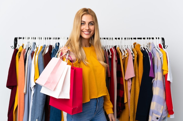 Jonge blonde vrouw in een kledingwinkel en met boodschappentassen die veel glimlachen