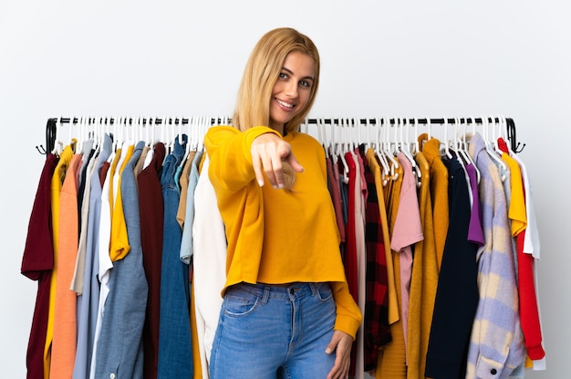 Foto jonge blonde vrouw in een kledingwinkel wijst met een zelfverzekerde uitdrukking naar je