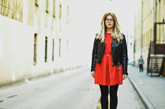 Jonge blonde vrouw in rode jurk poseren in de stad