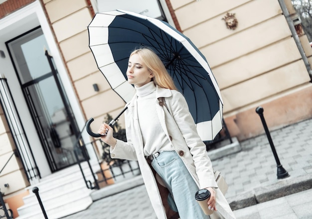 Jonge blonde vrouw in trenchcoat met paraplu in de stad