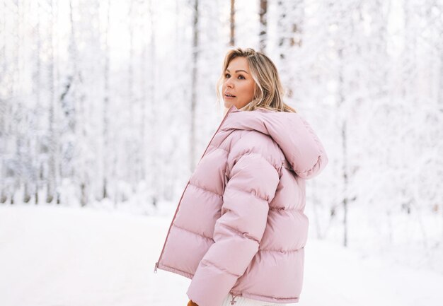 Jonge blonde vrouw in winterkleren wandelen in het besneeuwde winterbos