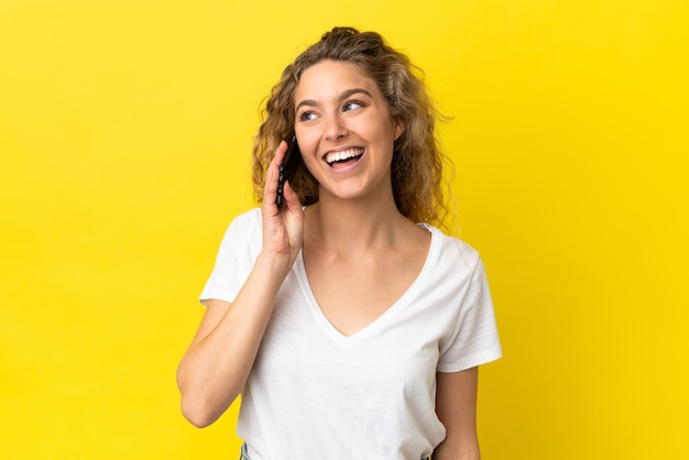 Jonge blonde vrouw met behulp van mobiele telefoon geïsoleerd op gele achtergrond op zoek naar kant