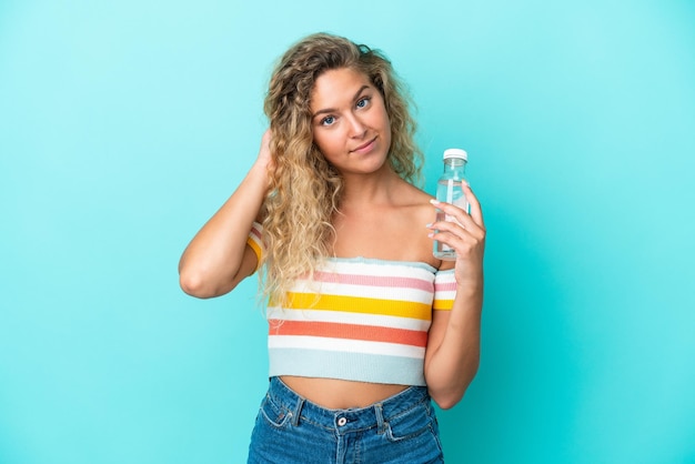 Jonge blonde vrouw met een fles water geïsoleerd op blauwe achtergrond twijfels