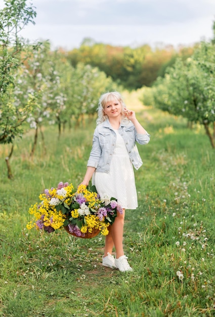 Jonge blonde vrouw met een grote mand met bloemen in de lentetuin Een meisje loopt met bloemen in het park