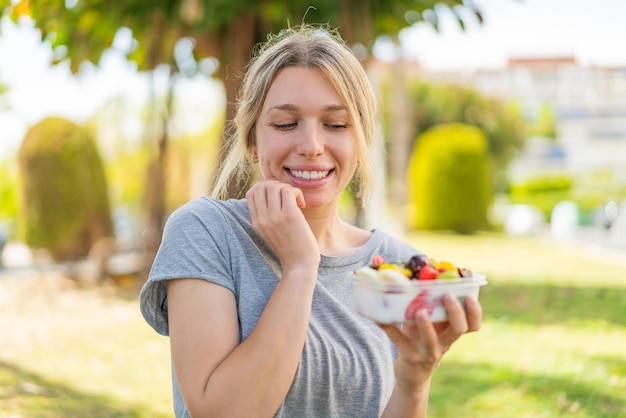 Jonge blonde vrouw met een schaal met fruit in de open lucht