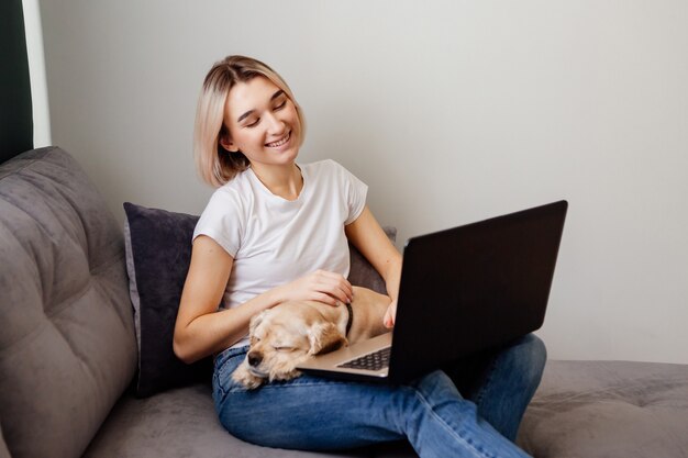 jonge blonde vrouw met een spaniel die aan een laptopblogger zit die aan het internet thuiskantoor werkt