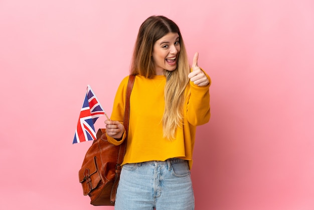 Jonge blonde vrouw met een vlag van het Verenigd Koninkrijk geïsoleerd op een witte muur met duimen omhoog omdat er iets goeds is gebeurd