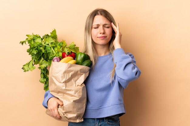 Jonge blonde vrouw met een zak vol groenten over geïsoleerde muur ongelukkig en gefrustreerd met iets