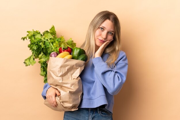 Jonge blonde vrouw met een zak vol groenten over geïsoleerde ongelukkig en gefrustreerd