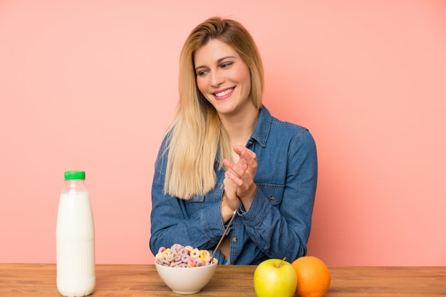 Jonge blonde vrouw met kom van granen applaudisseren