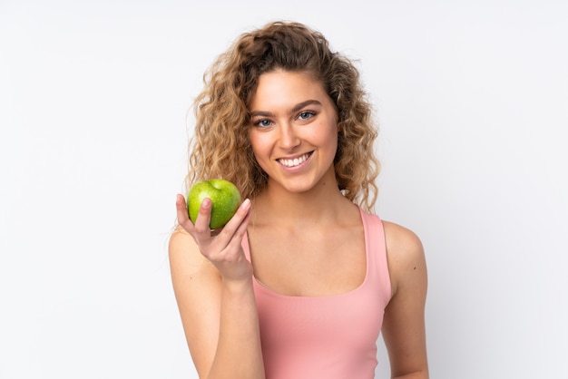 Jonge blonde vrouw met krullend haar op een witte muur met een appel