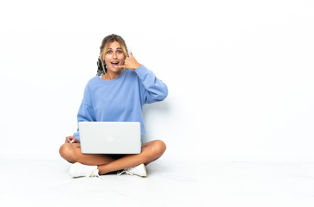 Jonge blonde vrouw met laptop geïsoleerd telefoongebaar maken