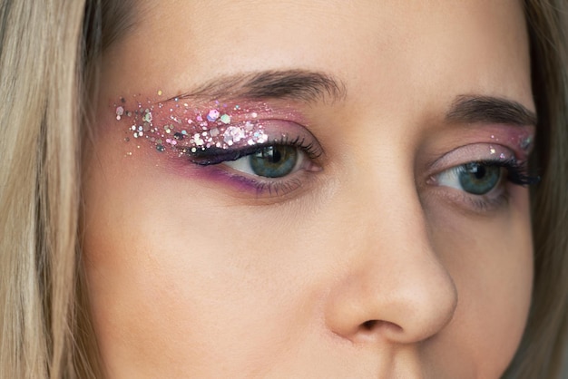 Jonge blonde vrouw met paarse en roze oogschaduw en glitter op de oogleden feestelijke oogmake-up