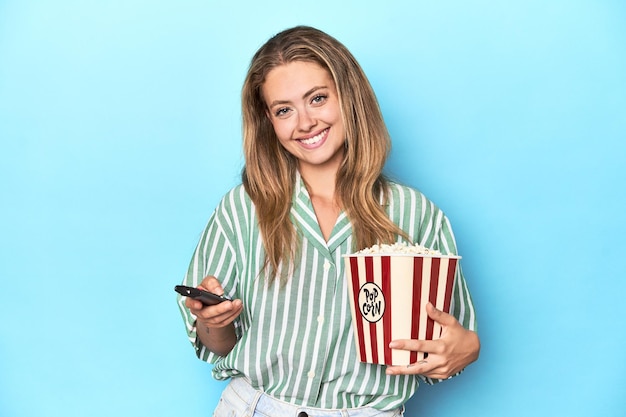 Jonge blonde vrouw met popcorn en een tv-afstandsbediening in een studio