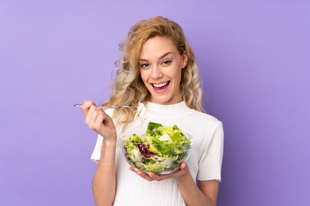 Jonge blonde vrouw met salade op paars