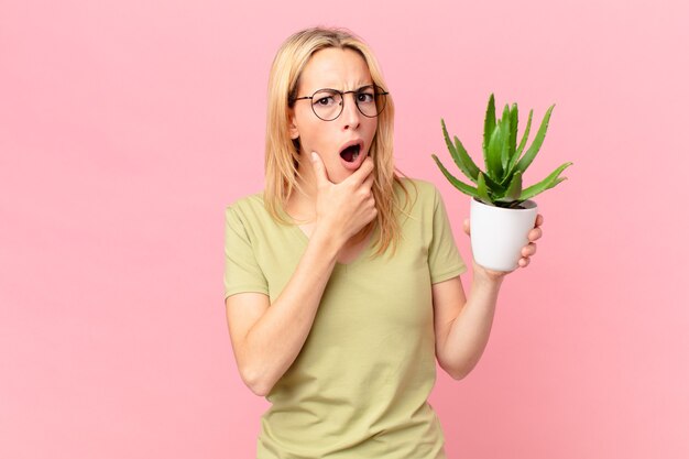 Jonge blonde vrouw met wijd open mond en ogen en hand op kin en met een cactus