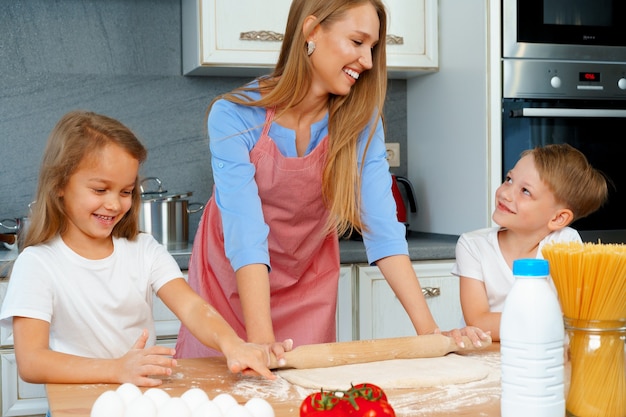 Jonge blonde vrouw, moeder en haar kinderen plezier tijdens het koken van deeg