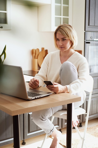 Jonge blonde vrouw online kopen met een creditcard op de laptop, thuis winkelen