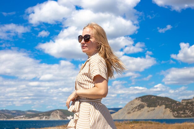 Jonge blonde vrouw op de achtergrond van de zee en de bergen op een zonnige zomerdag Reizen en toerisme