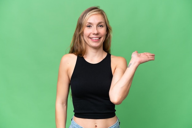 Jonge blonde vrouw over geïsoleerde achtergrond met denkbeeldige copyspace op de handpalm om een advertentie in te voegen