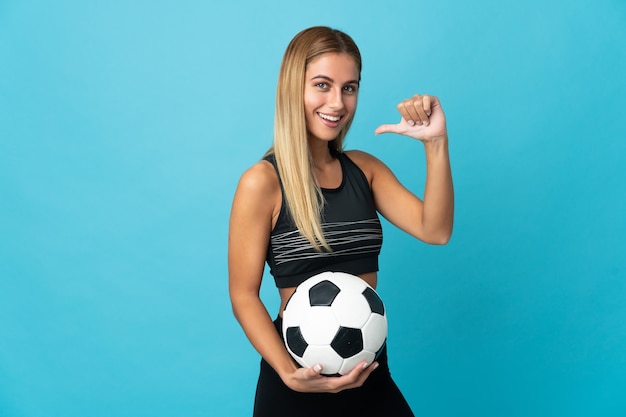 Jonge blonde vrouw over geïsoleerde ruimte met voetbal en trots op zichzelf