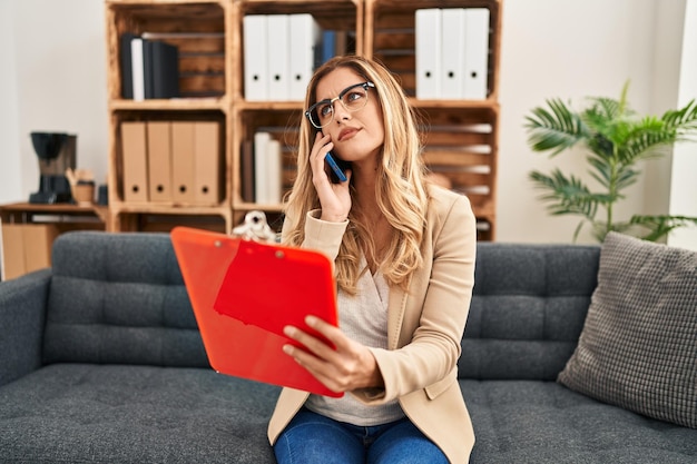 Jonge blonde vrouw psycholoog praten op de smartphone op psychologie centrum