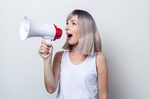 Jonge blonde vrouw schreeuwt in een megafoon op een lichte achtergrond.