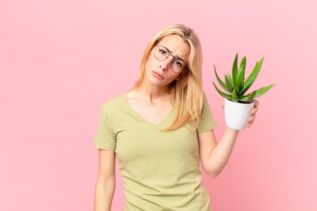 Jonge blonde vrouw voelt zich verdrietig en zeurt met een ongelukkige blik en huilt en houdt een cactus vast