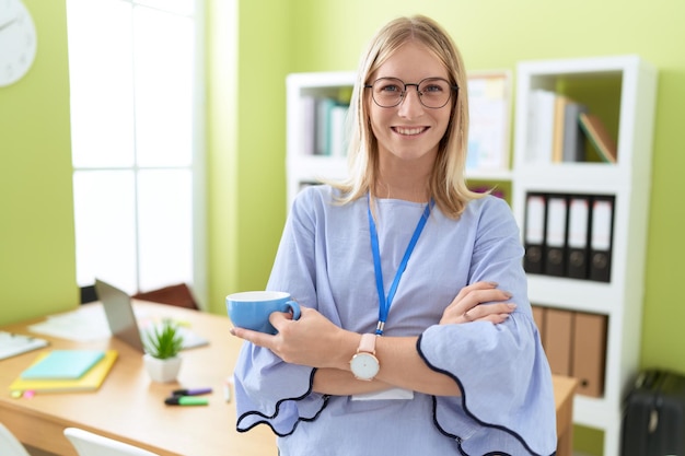 Jonge blonde vrouw zakelijke werknemer glimlachend zelfverzekerd koffie drinken op kantoor