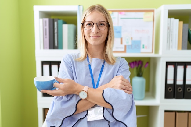 Jonge blonde vrouw zakelijke werknemer glimlachend zelfverzekerd koffie drinken op kantoor
