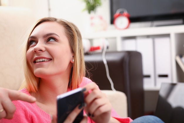 Foto jonge blonde vrouw zitten op de bank houden smartphone in handen