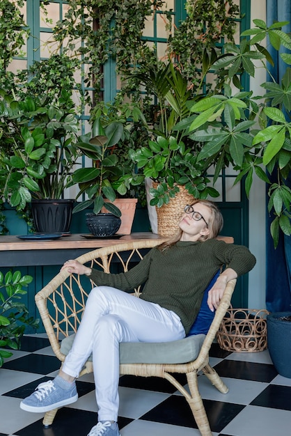 Jonge blonde vrouw zittend in een comfortabele stoel omringd met planten