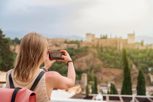 Foto jonge blonde vrouwelijke toerist die de foto neemt van het alhambra in granada, spanje