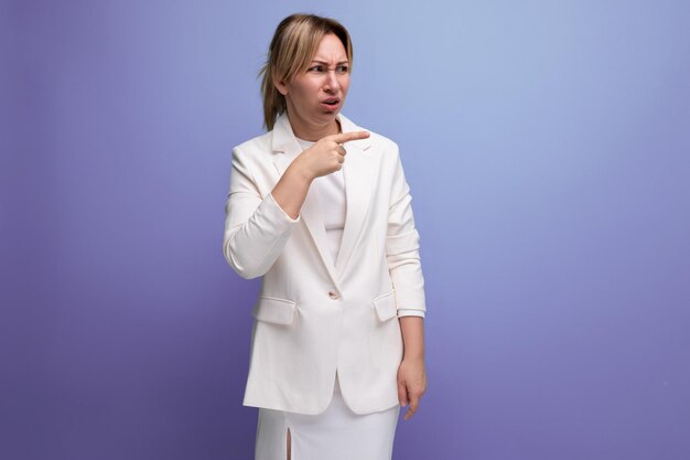 Jonge blonde werkgever vrouw in een witte elegante jas en rok kijkt minachtend naar de zijkant