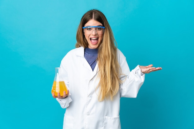 Jonge blonde wetenschappelijke vrouw die op blauwe achtergrond met geschokte gezichtsuitdrukking wordt geïsoleerd