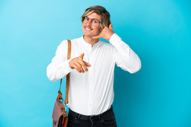 Jonge blonde zakenman die op blauwe muur wordt geïsoleerd die telefoongebaar maakt en voorzijde richt