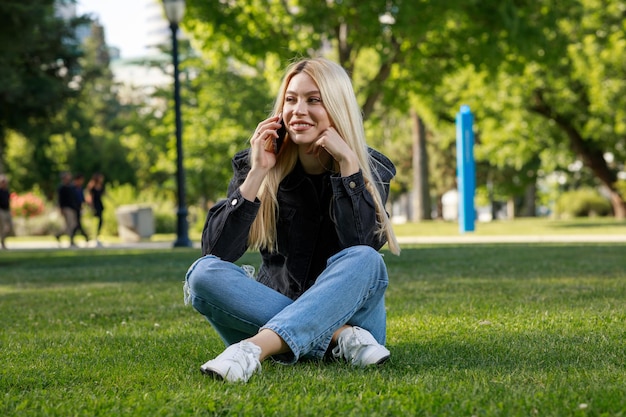 Jonge blonde zit in het park en praat aan de telefoon