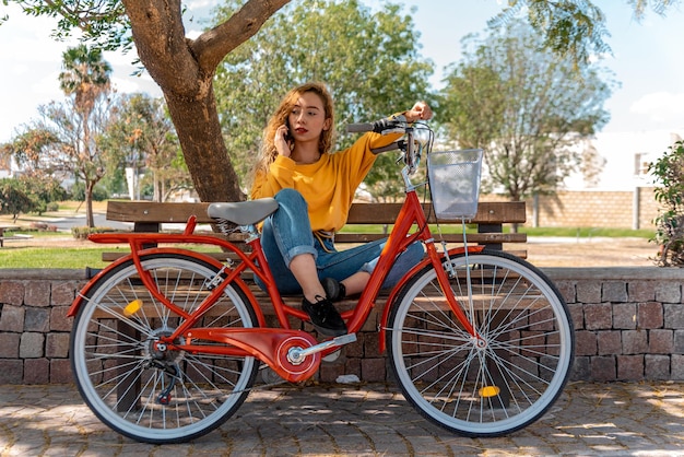 Jonge blonde zittend op een bankje, rustend in het park met haar fiets