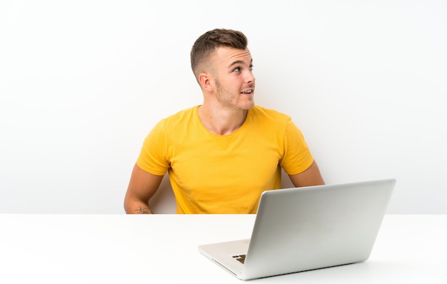 Jonge blondeman in een tafel met een laptop lachen en opzoeken